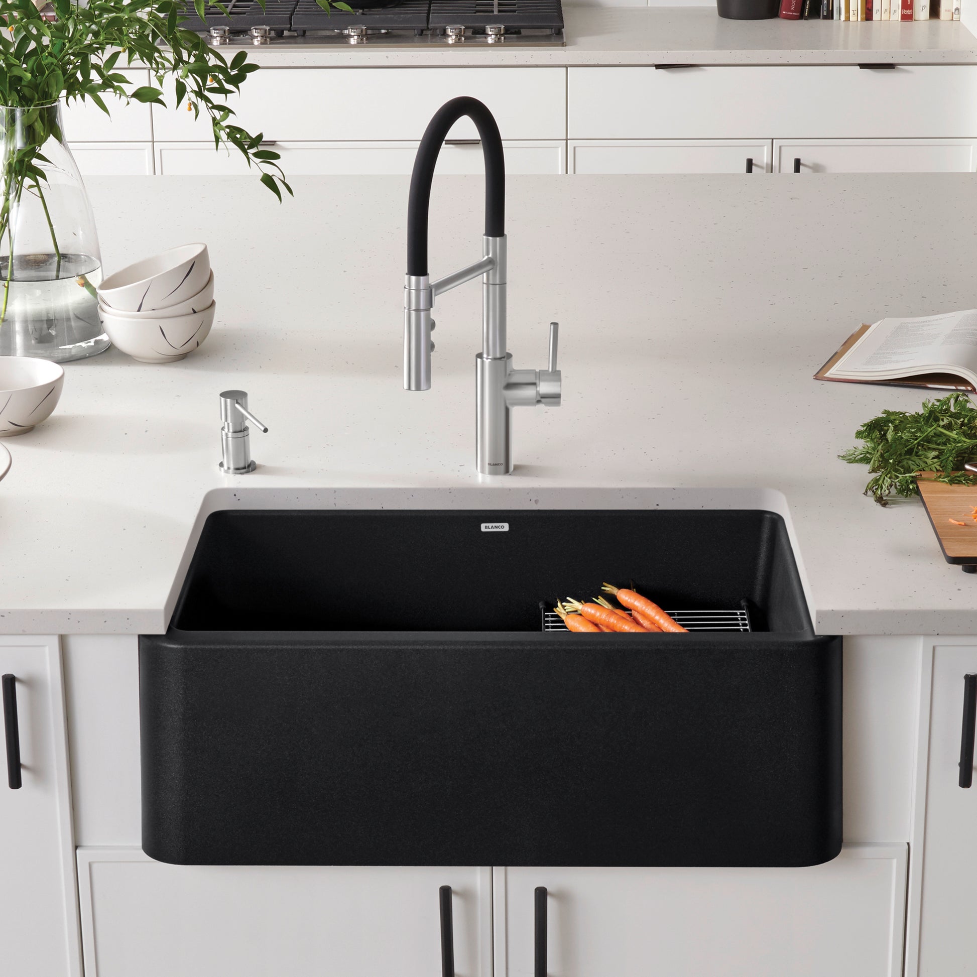 Anthracite apron front sink with stainless steel faucet and black pull-down sprayer installed in white kitchen countertop.