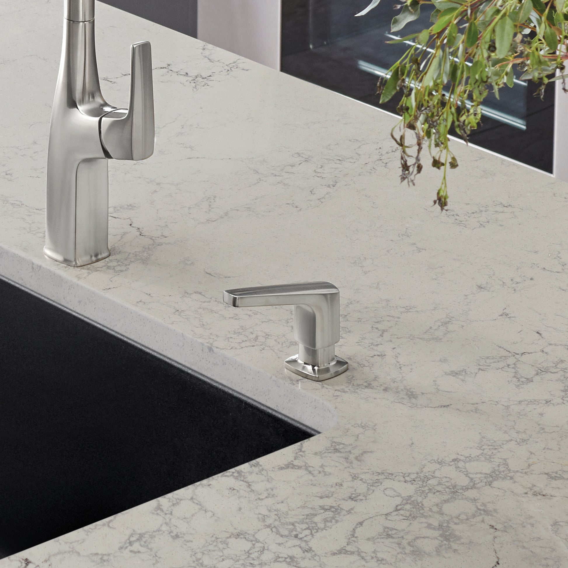 Stainless steel soap dispenser with rectangular pump head mounted on marble countertop next to kitchen sink.