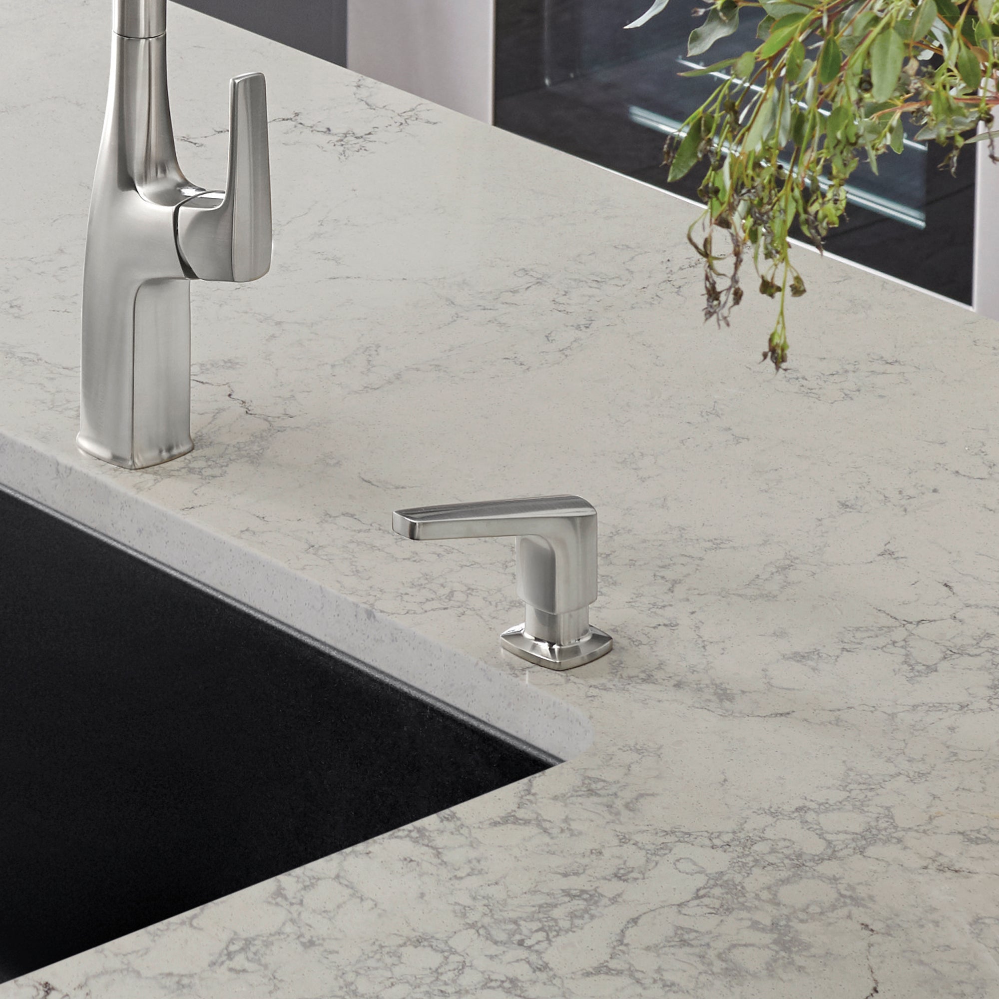 Stainless steel soap dispenser with rectangular pump head mounted on marble countertop next to kitchen sink.