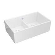 White fireclay double bowl apron front kitchen sink with low center divider and drain holes.