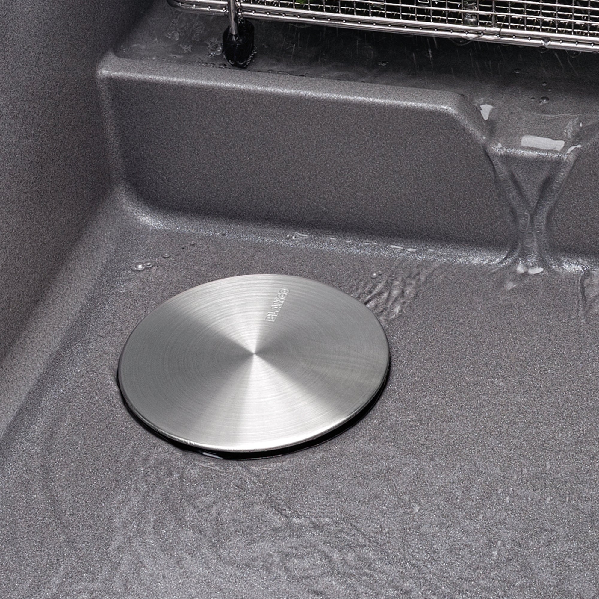 Stainless steel circular drain cover with brushed finish installed in a kitchen sink basin.