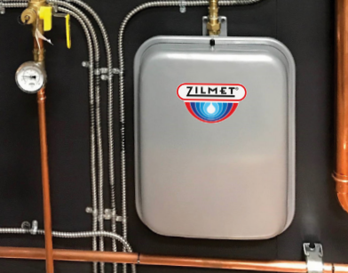 Silver rectangular hydronic expansion tank with Zilmet logo mounted on wall with connected copper and flexible tubing.