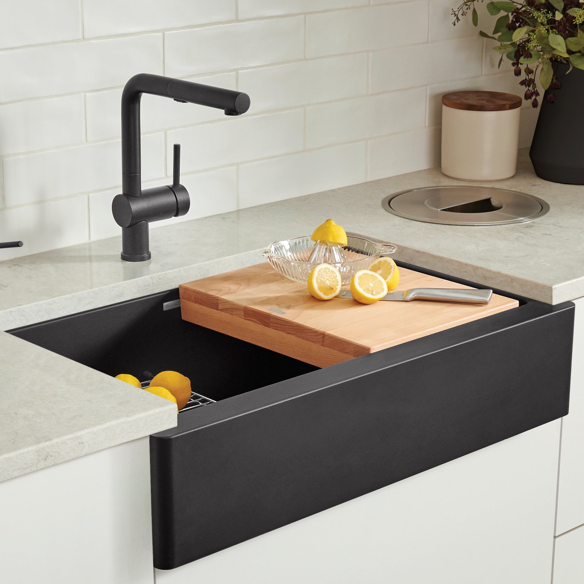 Beechwood cutting board resting across black apron front sink with lemon slices and juicer on surface.