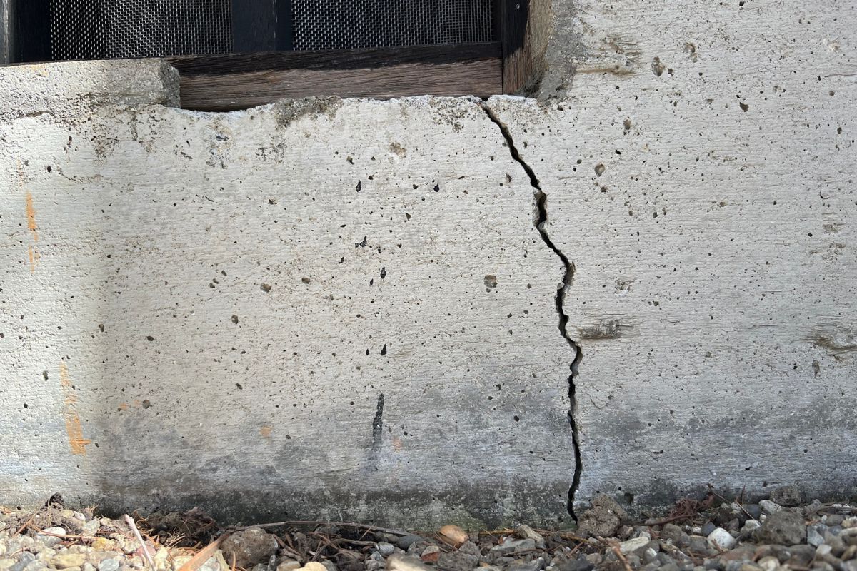 Inspect foundation and walls: A closeup of the foundation of a home with a large crack running across the concrete