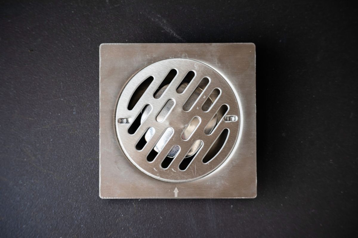 Clean and Inspect Floor Drains A closeup image of a stainless steel floor drain installed on a black bathroom floor
