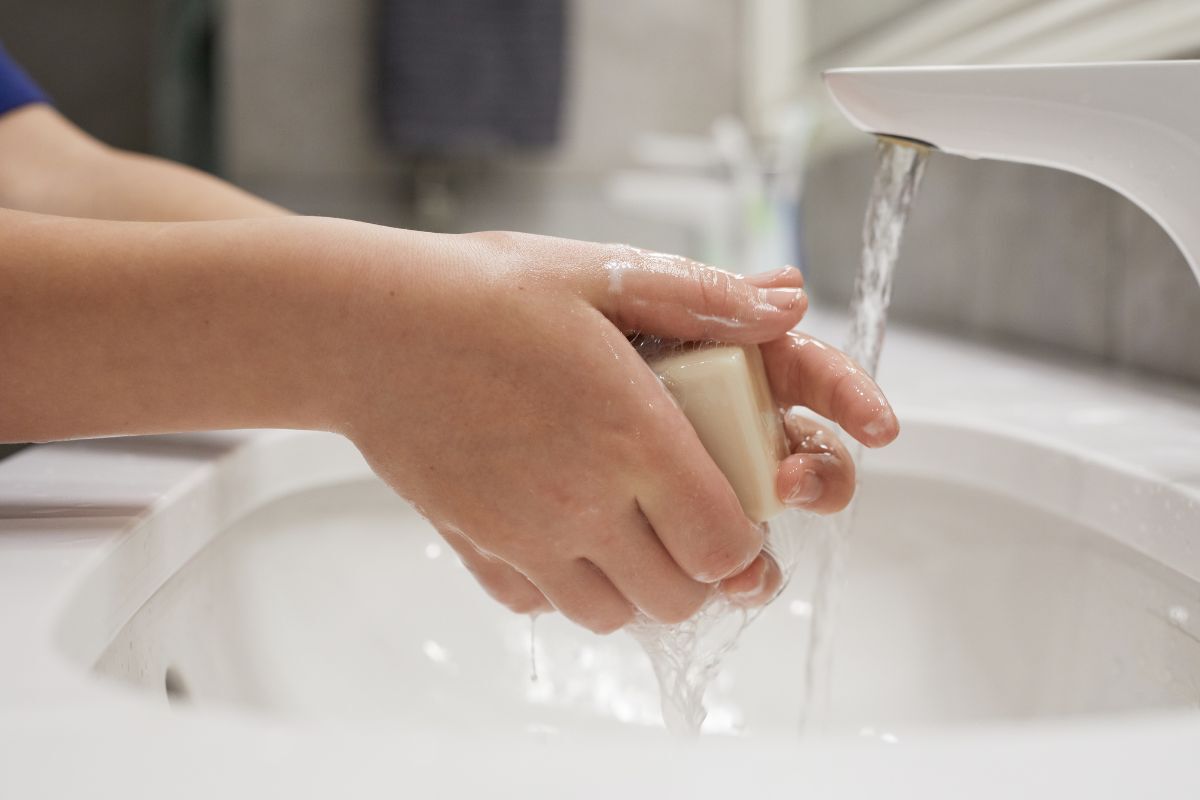 A child washing their hands with soap over a white sink using a touchless bathroom faucet