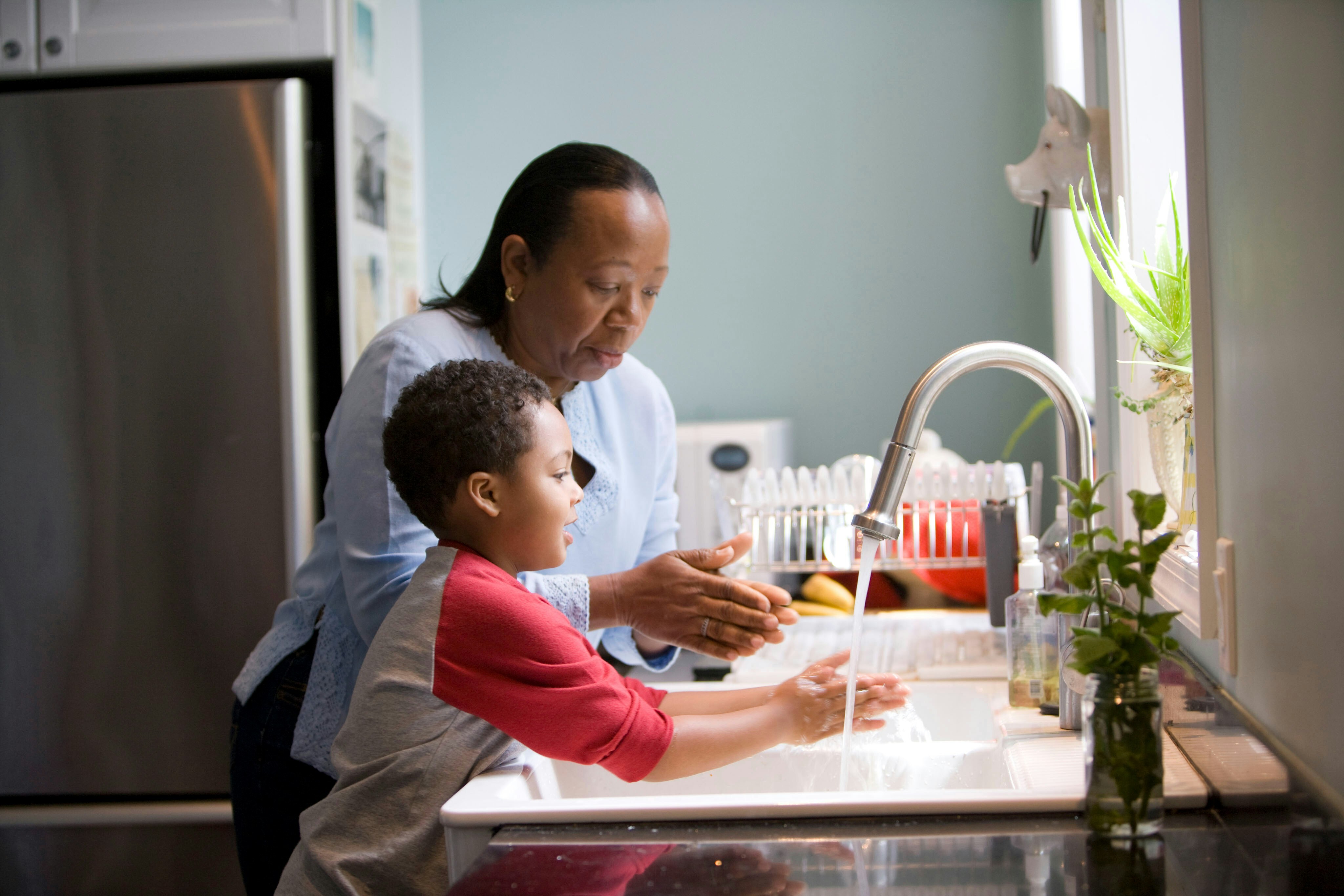 Increased Household Water Usage An older woman with her young grandson standing at the sink washing dishes