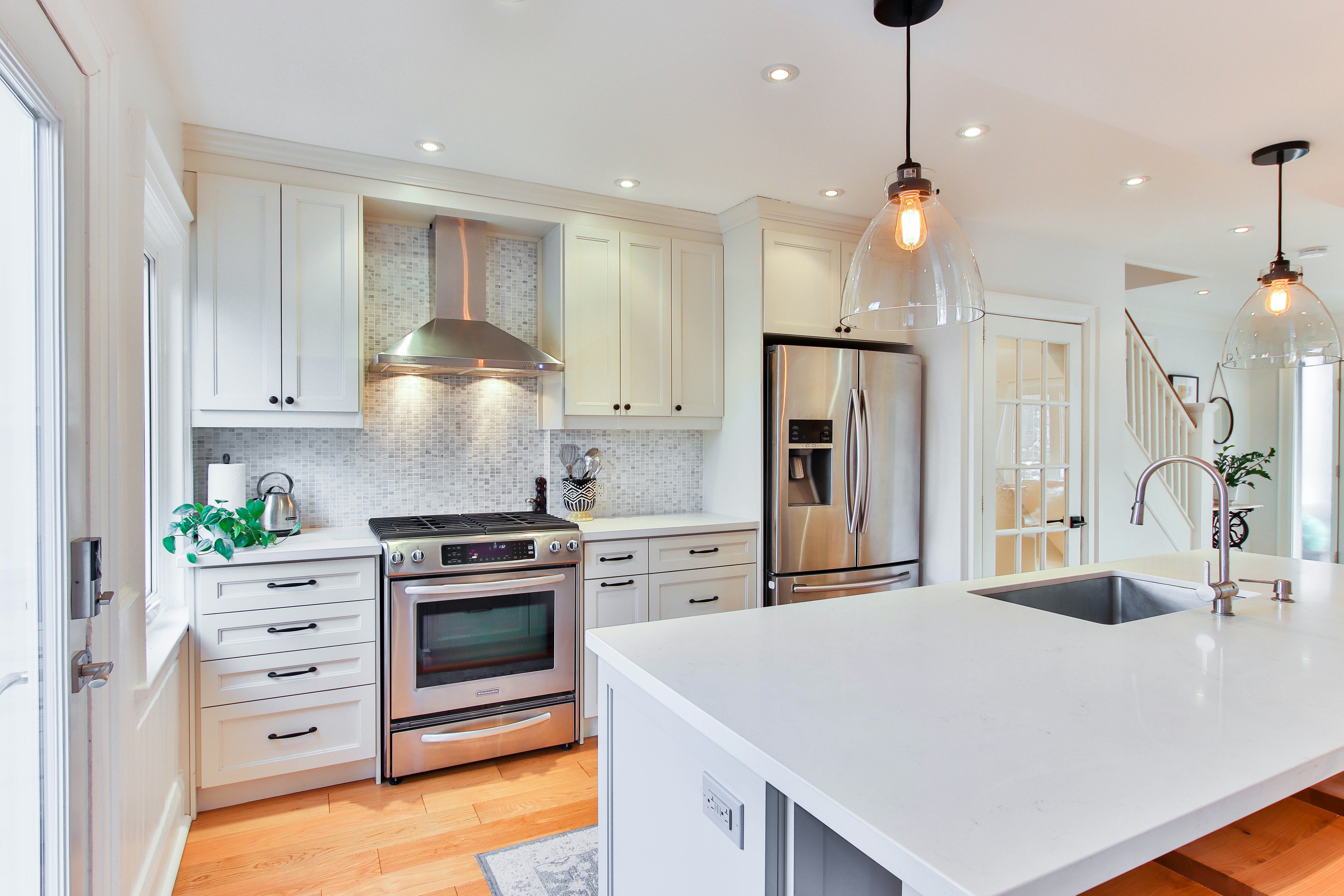 A modern, white kitchen with bright lights reflecting the stainless steel decorative plumbing