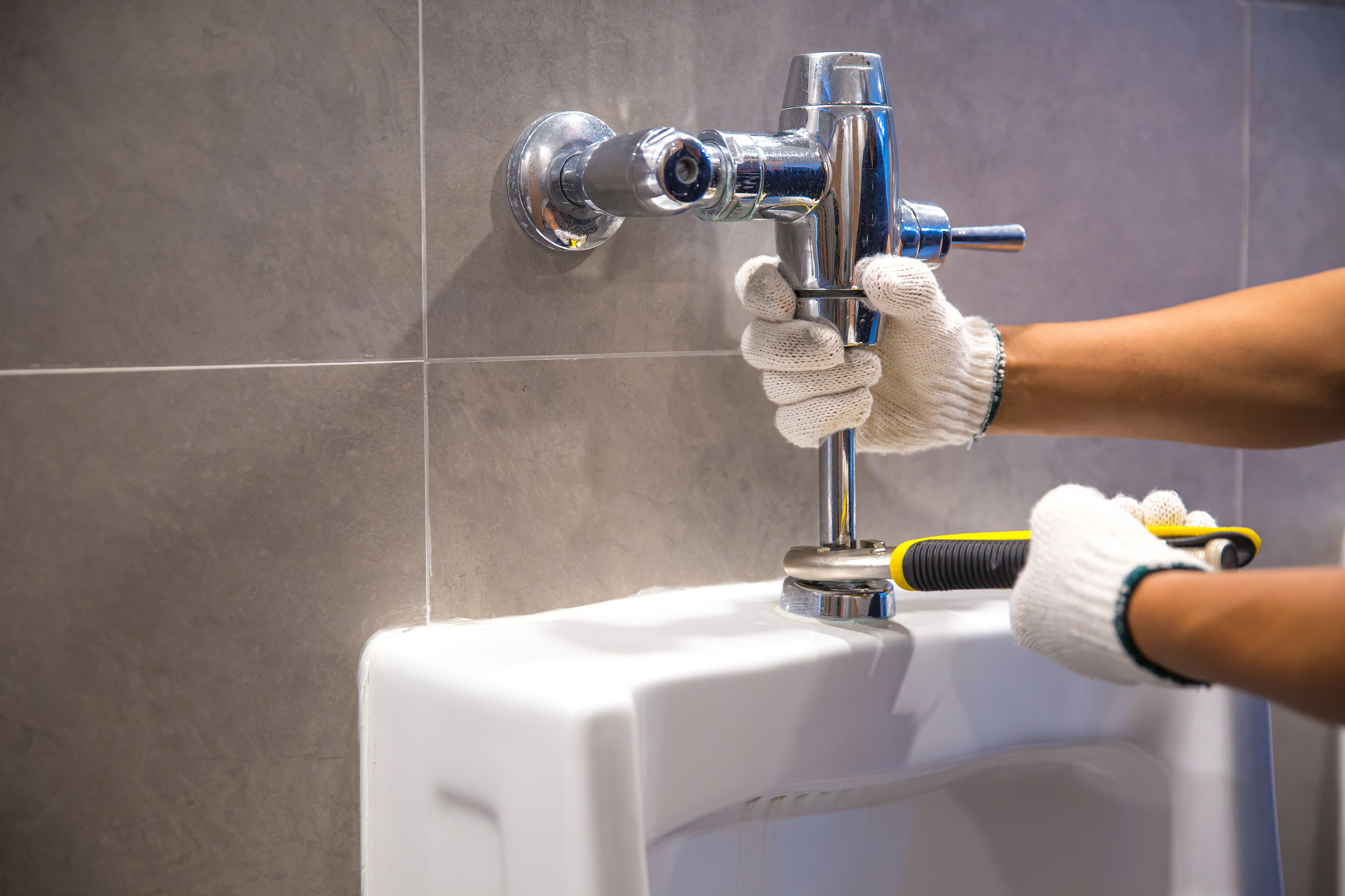 Running or Leaking Toilets A gloved hand holding onto the silver pipes on top of a urinal