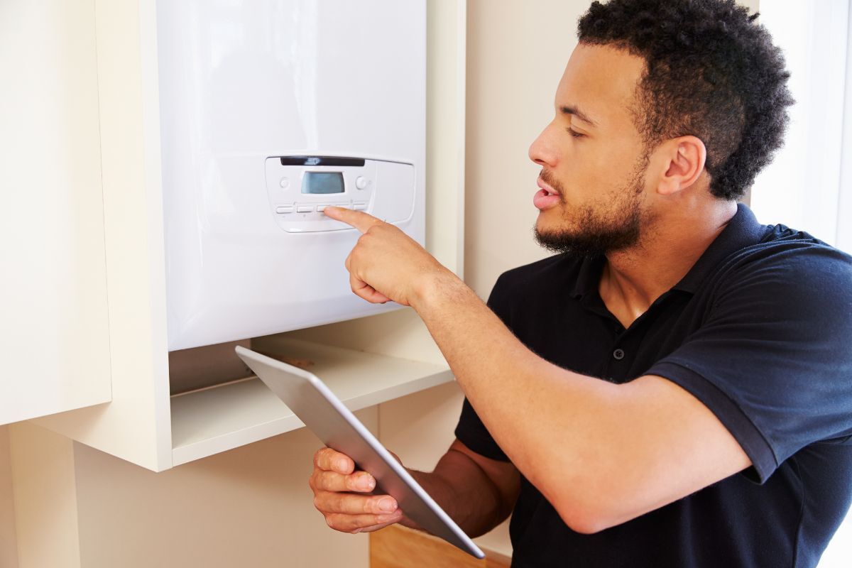A plumber servicing a boiler mounted on the wall and using an iPad to take notes.