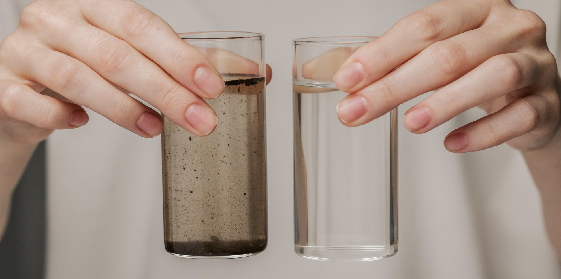Hands holding a dirty glass of water on the right and a clean glass of water on the left